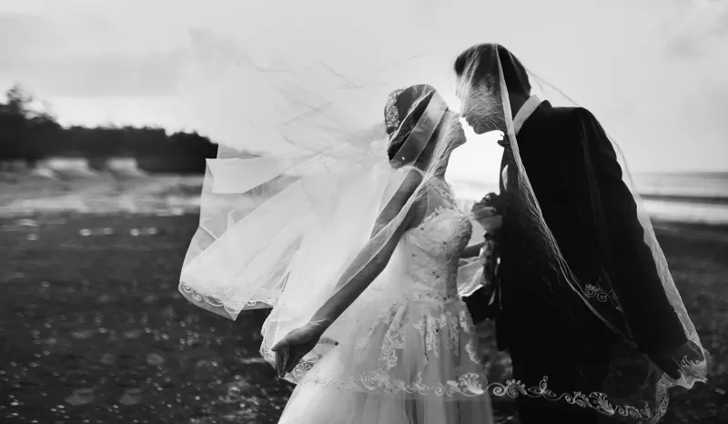 Black-and-white photo of a bride and groom sharing a kiss by the sea