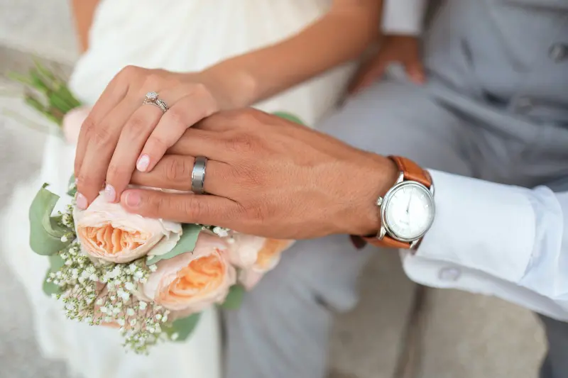 Bride and groom holding hands over a bouquet of peach roses
