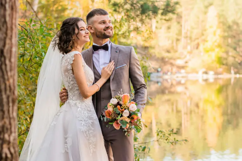 Bride and groom smiling together by a lake at golden hour